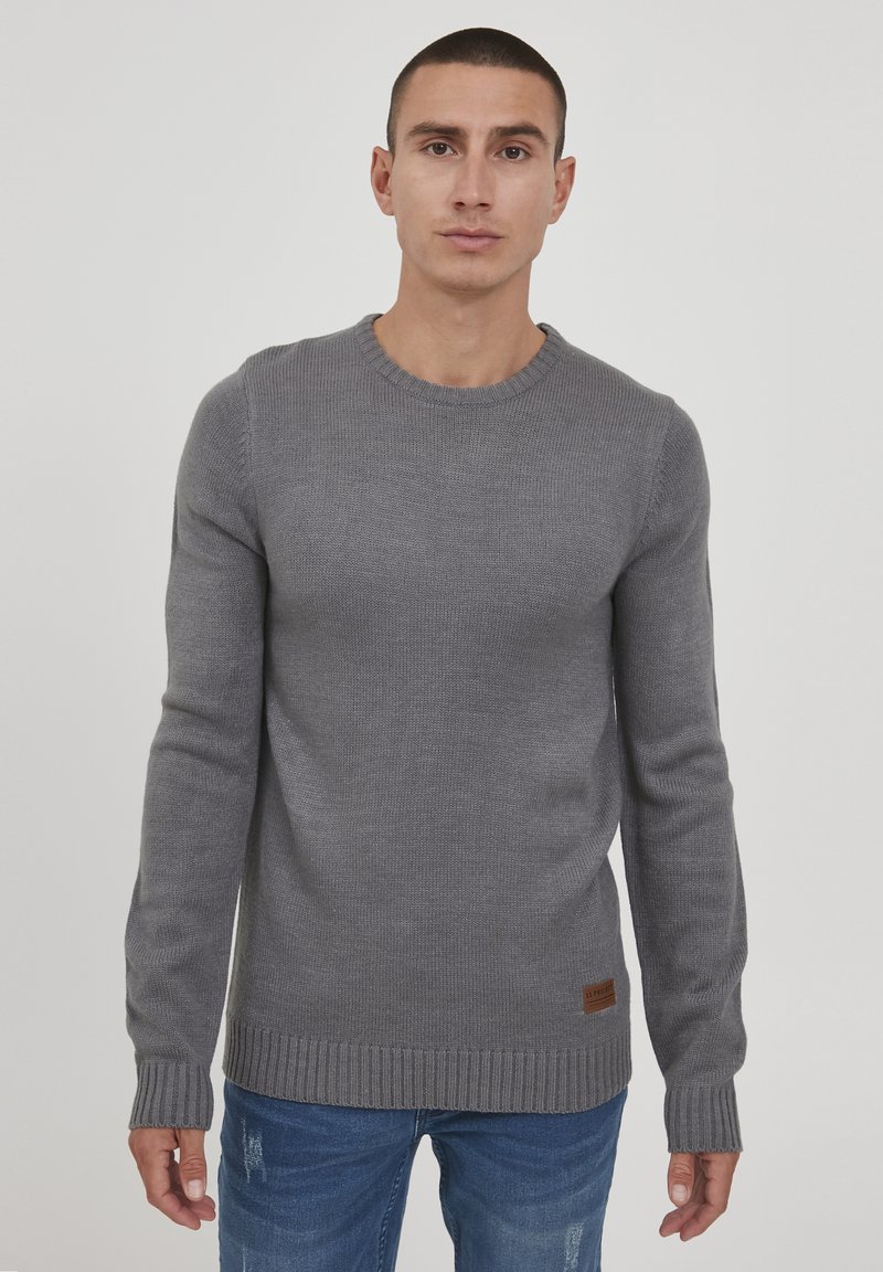 Grijze gebreide trui met een ronde halslijn, ribgebreide manchetten en zoom. Bevat een textiele stof en een klein leren merklabel onderaan.