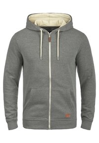 Šedá mikina na zip vyrobená z měkkého materiálu, s krémovým vnitřkem, kapucí se šňůrkami a dvěma předními kapsami.