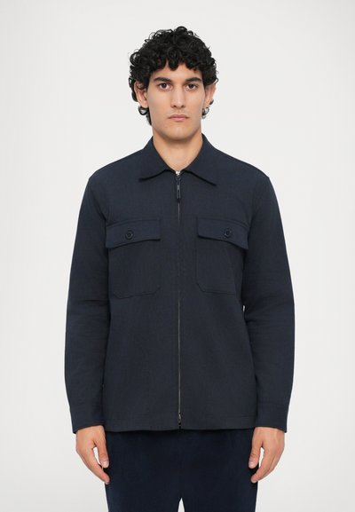 Chaqueta azul marino con cremallera, fabricada con tejido texturizado, que presenta un cuello, dos bolsillos en el pecho con solapas y mangas largas. Diseño sencillo.