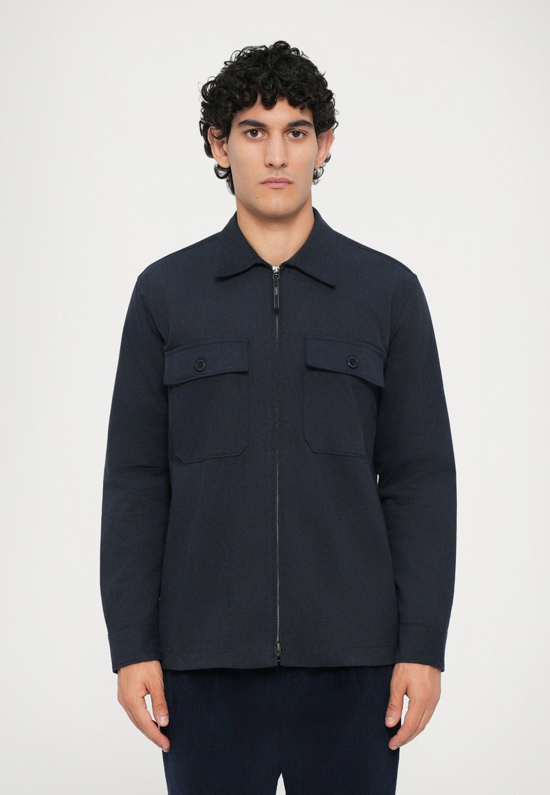 Navy blue zip-up jacket made from a textured fabric, featuring two front chest pockets with flap closures and a pointed collar.