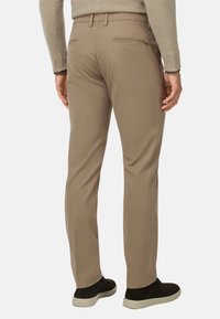 Pantalones de color beige claro con un corte ajustado, que presentan una textura suave, dos bolsillos traseros con cremallera y un diseño limpio en la cintura.