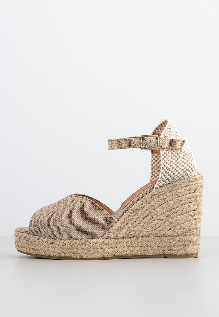 Beige Espadrille-Wedgesandale aus Stoff mit einem geflochtenen Absatz. Verfügt über einen Knöchelriemen und ein offenes Zehen-Design, akzentuiert durch strukturiertes Geflecht.