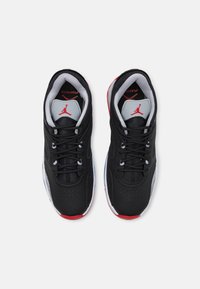 Svarta sportskor har en slät syntetisk ovandel, grå detaljer, röd häl och en vit sula med ett texturerat mönster. Skosnörena är mörkgrå.