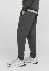 Dark gray sweatpants made of soft material, featuring side pockets and a tapered leg design, paired with silver athletic shoes.