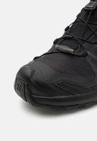 Black trail running shoe with a textured upper, reinforced toe cap, and integrated lacing system; features a durable rubber outsole.