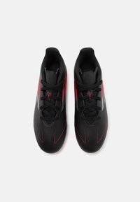 Scarpe da ginnastica nere con accenti e strisce rosse, caratterizzate da una texture rigata e design con lacci. Forma aerodinamica per migliori prestazioni.