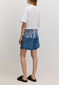Wit cropped t-shirt met een geknoopte franjerand aan de onderkant, gecombineerd met blauwe denim shorts en zwarte slip-on sandalen.