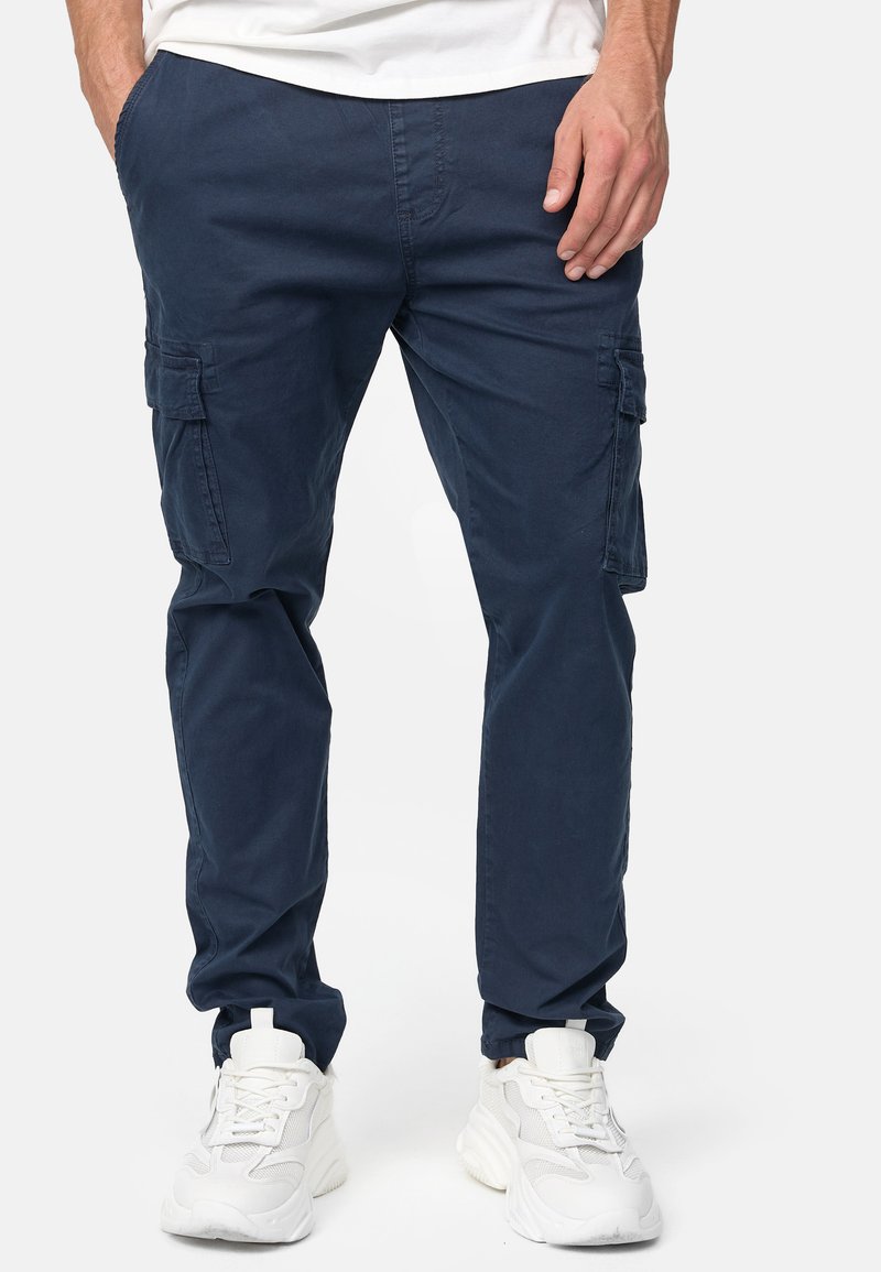 Granatowe spodnie cargo wykonane z bawełny, z bocznymi kieszeniami, tapered fit i elastycznymi mankietami na kostkach, w zestawieniu z białymi sneakersami.