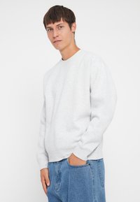 Un sweatshirt gri deschis cu decolteu rotund și mâneci lungi, confecționat dintr-un material moale. Asortat cu pantaloni din denim albastri, având un buzunar lateral.