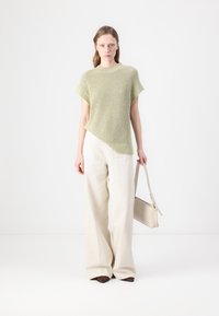 Top de punto verde claro con mangas cortas y dobladillo asimétrico, combinado con pantalones de pierna ancha beige. La modelo sostiene un bolso claro.