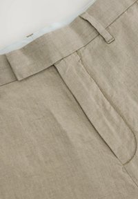 Béžové lněné kalhoty s plochým opaskem, jemným leskem a bočními kapsami s čistým šitím a minimalistickým designem.