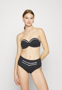 Crni bikini set s bez naramenica topom sa nabrano tkaninom i bijelim detaljima, uparen s visokim donjim dijelom ukrašenim okruglim detaljem.