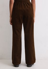 Bruine corduroy wijde pijpen met een elastische tailleband, voorzien van verticale ribbelstructuur en afgewerkte randen. Geschikt voor casual kleding.