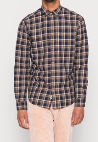 Camisa de manga larga a cuadros en azul marino y beige con cuello abotonado, un bolsillo en el pecho y dobladillo curvado, hecha de tela a cuadros.