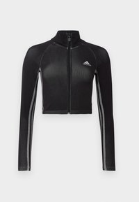 Musta lyhyt vetoketjullinen takki, jossa on pitkät hihat, raglan-muotoilu, heijastavat yksityiskohdat ja korkea kaulus. Takissa on Adidas-logo rinnassa.