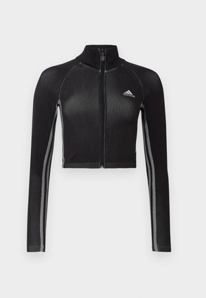 Crna skraćena jakna na zip s dugim rukavima, raglan dizajn, reflektirajući detalji i visoki ovratnik. Sadrži Adidas logo na prsima.