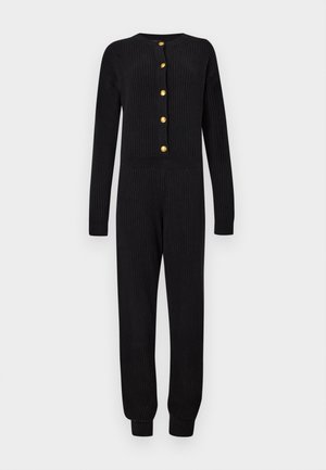 Combinaison noire en maille côtelée à manches longues avec boutons dorés sur le devant et chevilles côtelées.