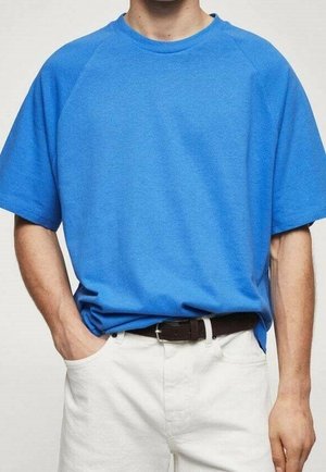 T-shirt bleu à manches courtes en tissu doux avec un col rond et des manches raglan, associé à un pantalon blanc et une ceinture noire.