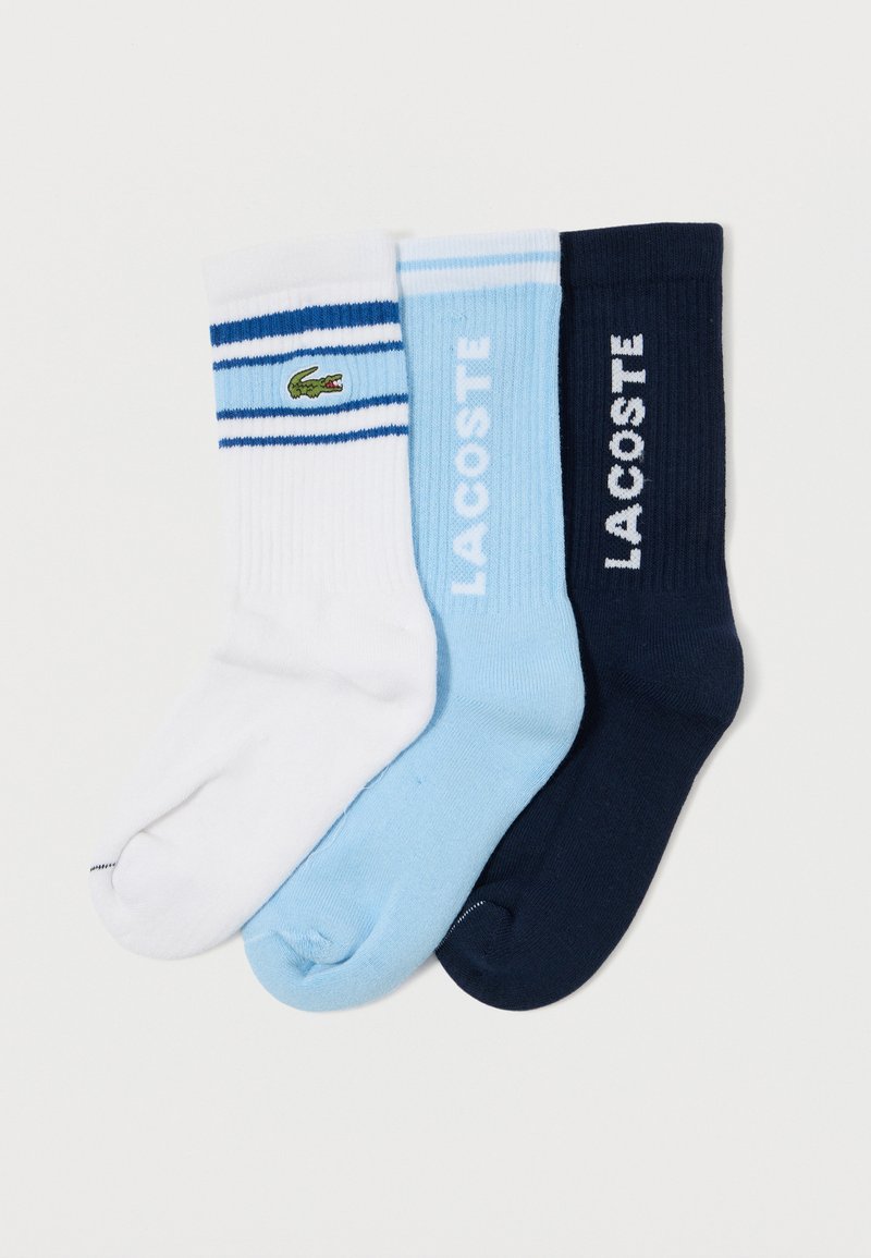 Trei perechi de șosete din bumbac: albe cu dungi albastre și logo-ul unui crocodil verde, bleu deschis și bleumarin închis, având textură ribată și logo.