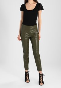 Czarny bodysuit z krótkim rękawem i okrągłym dekoltem, połączony z oliwkowymi spodniami ankle z faux skóry oraz czarnymi sandałami na obcasie z sznurowaniem.