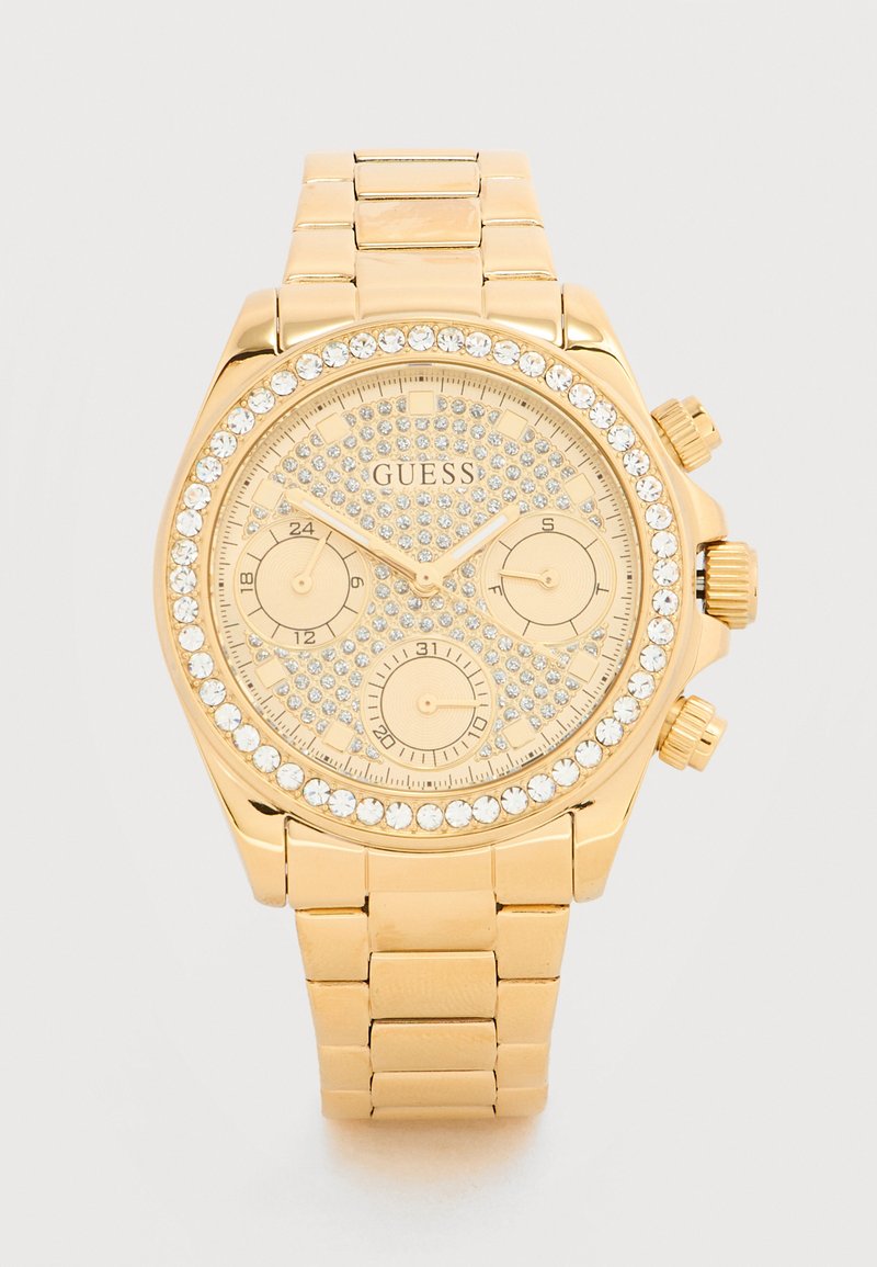 Ρολόι χειρός Guess σε χρυσή απόχρωση με διακοσμήσεις από κρύσταλλα, τρεις μικρομετρητές για λειτουργίες 24 ωρών, ημερομηνίας και ημέρας, και μπρασελέ από μεταλλικούς κρίκους.