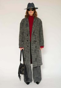 Manteau long à carreaux gris avec de grands revers, associé à un col roulé bordeaux, un pantalon en denim à larges jambes et un sac à bandoulière noir.