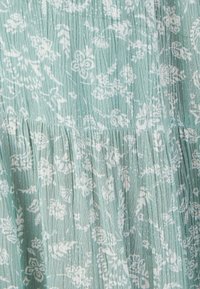 Tissu bleu clair présentant un motif floral blanc avec des plis et une finition texturée. Le design offre une apparence douce et délicate.