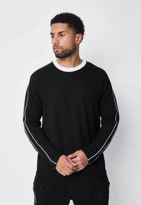 Sweatshirt noir à manches longues avec un col rond blanc et des rayures blanches sur les côtés. Fabriqué dans un tissu doux avec une coupe décontractée.