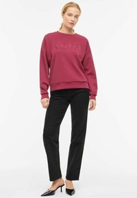 Sweatshirt bordeaux avec texte "LOVE" en relief, associé à un jean noir droit et des mules à talons noires. Tenue simple et décontractée.
