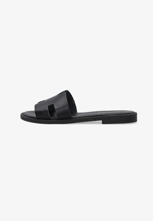 Schwarze flache Slide-Sandale mit breitem Lederriemen mit rechteckigen Ausschnitten und strukturierter Sohle, Seitenansicht vor weißem Hintergrund.