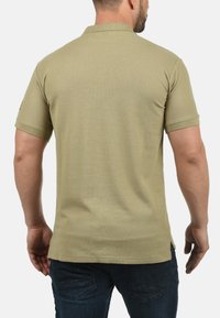 Khaki polo-shirt med ribbet krave og korte ærmer. Bagsiden viser teksturen og pasformen. Bæret med mørkeblå denimjeans.