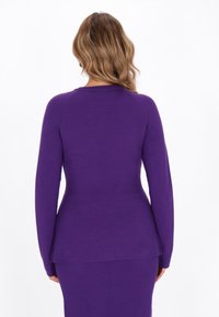 Lila hosszú ujjú felső peplum fazonnal, puha kötött anyagból készült. Kerek nyakkivágással és testre simuló ujjakkal rendelkezik.