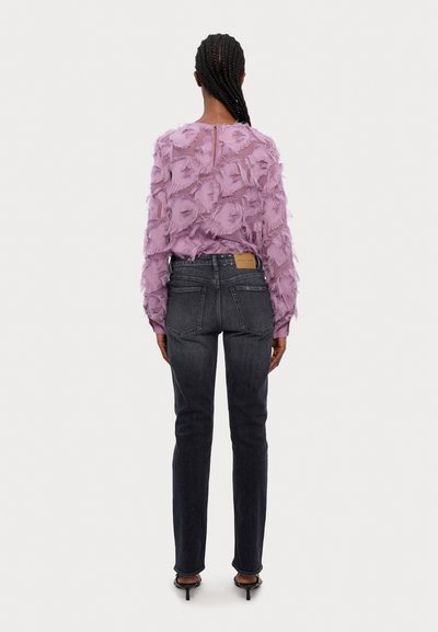 Top de tono lilac con textura y diseño elevado en forma de pétalos, combinado con jeans oscuros de mezclilla. El conjunto presenta un detalle en la parte posterior en forma de ojal y un corte ajustado.