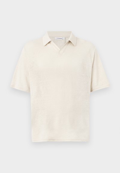Polo beige à manches courtes avec un col doux et une ouverture en V, présenté sur un fond gris clair uni.