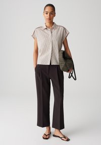 Camicia a maniche corte a righe beige e bianco sporco, abbinata a pantaloni neri a gamba larga e una borsa tessuta verde scuro. Sandali neri piatti.