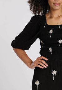 Vestido negro texturizado con mangas cortas abullonadas, con bordado de palmeras plateadas en el cuerpo y la falda, con un corte ajustado en la cintura.
