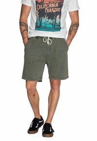 Olijfgroene shorts met een koord in de taille, zijzakken en een gestikte zoom. Gecombineerd met een witte graphic t-shirt met een kleurrijke print.