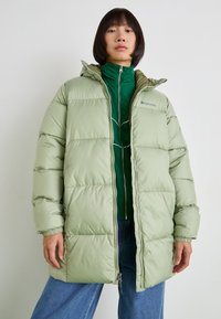 Jachetă puffer verde deschis, cu fermoar frontal, glugă și manșete elastice. Prezintă un design matlasat și este stratificată peste o jachetă verde cu fermoar.