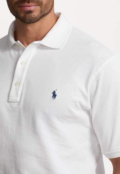 White polo shirt made of cotton, featuring a two-button placket and a navy embroidered logo on the left chest. Soft texture and classic fit.