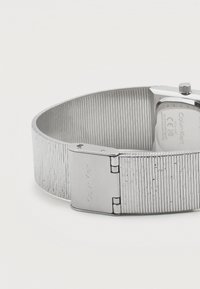 Ασημένιο ρολόι χειρός Calvin Klein με υφασμένη μεταλλική μπάντα και πόρπη χαραγμένη με το λογότυπο Calvin Klein.