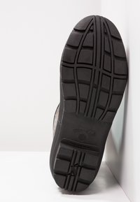 La suola nera della scarpa è realizzata in materiale gommoso con una superficie testurizzata, profondi modelli di battistrada e marchio. La forma è piatta con bordi arrotondati.