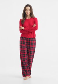 Red long-sleeve top paired with plaid pajama pants featuring red, black, and green colors. Soft fabric with a relaxed fit and wide leg.