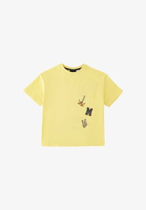 Maglietta gialla a maniche corte con taschino sul petto, con un piccolo fiore arancione, la lettera "M" e un grafico della mano con il segno di pace sotto la tasca.