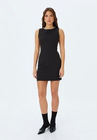 Abito nero senza maniche con una silhouette aderente, dettagli in perle attorno al collo, abbinato a calzini neri alla caviglia e décolleté a punta.