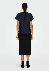 Top blu navy a maniche corte con una vestibilità ampia, abbinato a una gonna midi nera a coste. Stivaletti neri completano l'outfit.