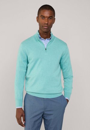 Suéter azul claro con cremallera, hecho de un tejido suave con un acabado texturizado, combinado con una camisa de rayas con cuello y pantalones azules.