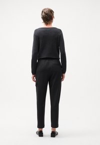 Pull en maille gris avec un décolleté large associé à un pantalon noir à rayures verticales avec des poches avant et une poche arrière, porté avec des chaussures noires.