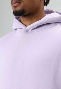 Lila capuchontrui met een zachte textuur en standaard pasvorm. Voorzien van een capuchon met trekkoord en subtiele stikseldetails.