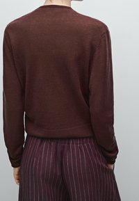 Bordeauxrode trui met lange mouwen en een ronde halslijn, met een gladde textuur. Gecombineerd met donkere broek met fijne strepen.