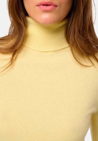 Weicher gelber Rollkragensweater aus Strickstoff, mit einer figurbetonten Passform und Rippstruktur am Kragen und an den Bündchen.